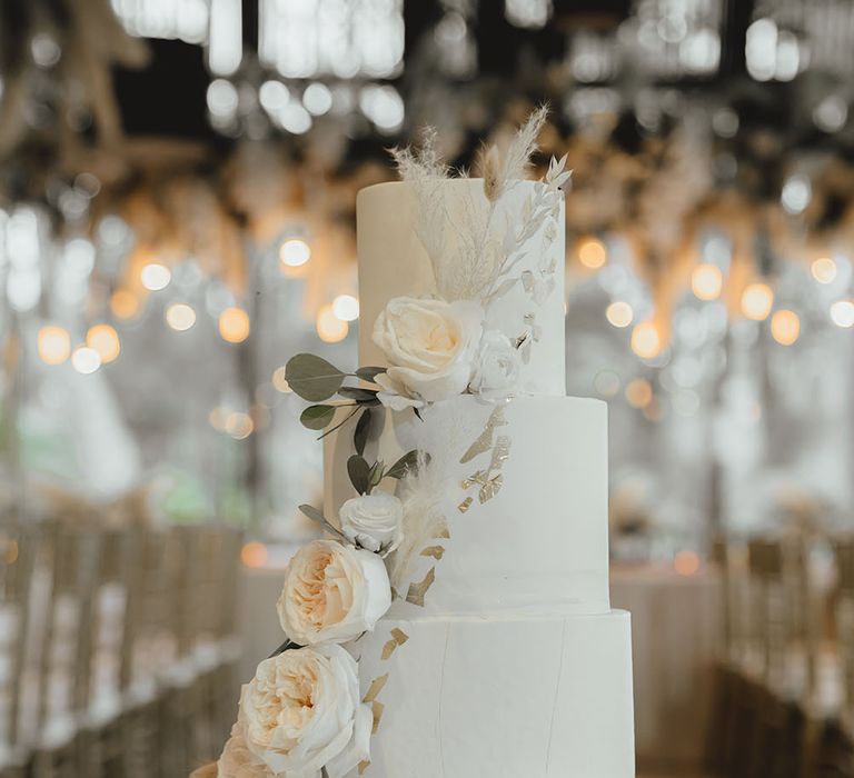 Four-tier wedding cake complete with white frosting and floral decoration with gold leaf 