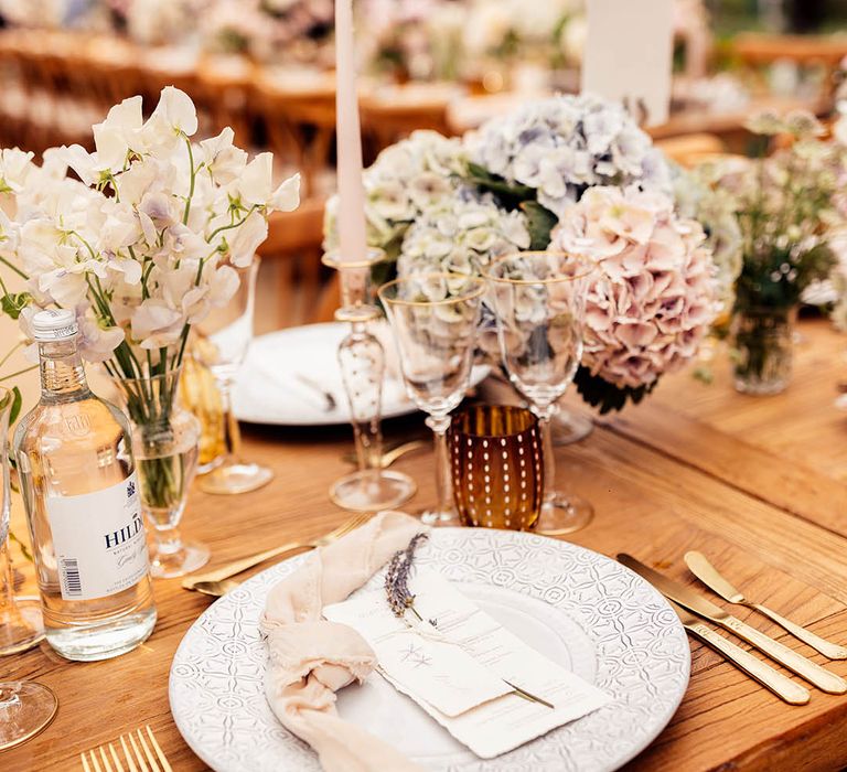 Pink taper candle with pastel hydrangea wedding flower arrangement for simple tablescape on a wooden banquet table 