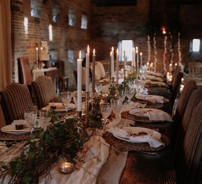 Rustic barn decorated with fairy lights and lit taper candles with crystal glassware and foliage decorating the table 