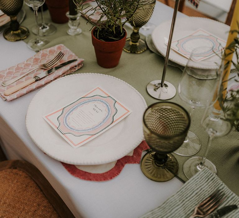 Green coloured glassware with a green table runner with a pink wedding menu and cream plates