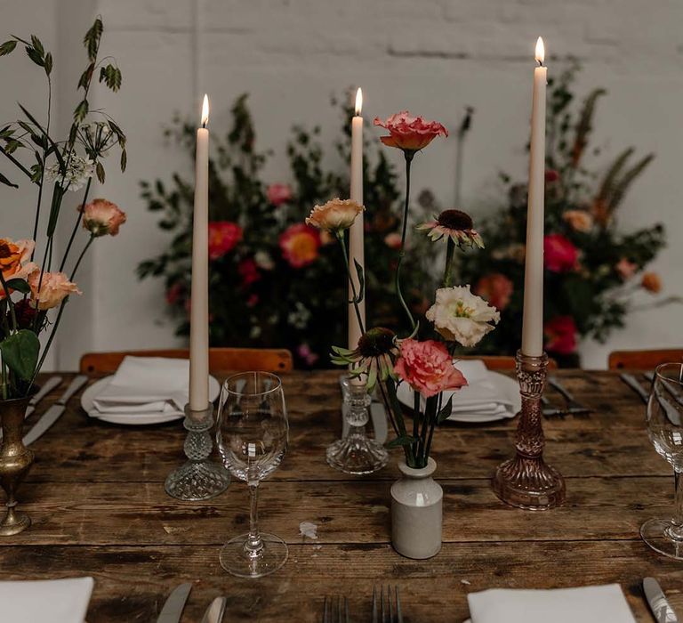 Three tapered ivory candles in clear and rose gold candle holders on neutral minimalistic wedding tablescape with pops of colourful flowers