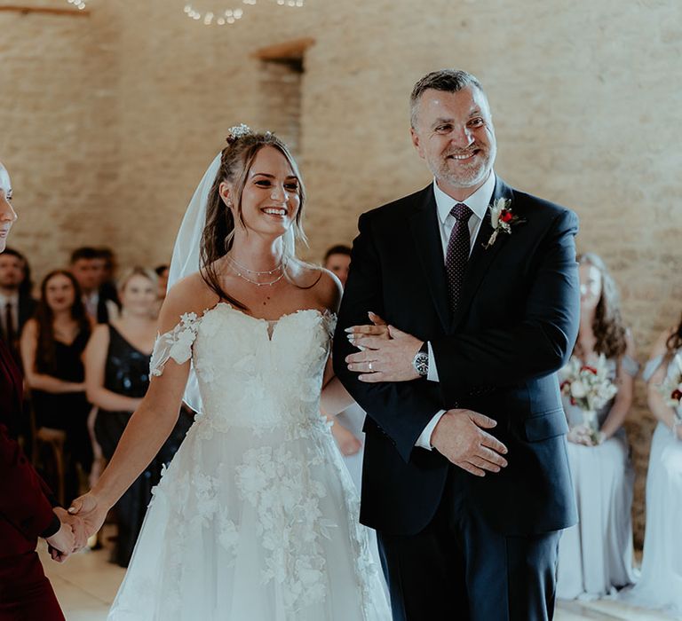 Father of the bride in a navy blue suit walks the bride in a flower wedding dress down the aisle to meet the bride in a burgundy suit 