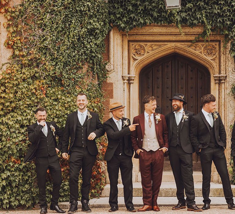 Groom in maroon suit stands outdoors with his groomsmen in black suits and pale blue ties