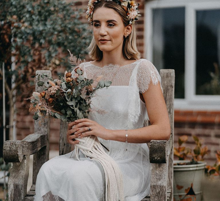 Bride in a boho sheer lace wedding dress holding a dried flower bouquet with macrame detail and dried flower headband 