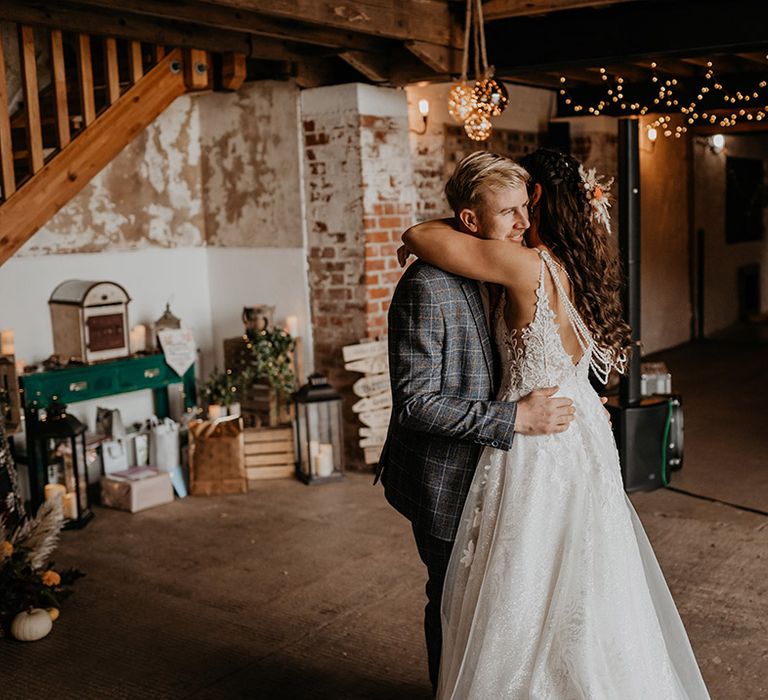 Bride in lace wedding dress with pearl back detail has a private dance with the groom in a grey three piece checkered suit and orange tie 