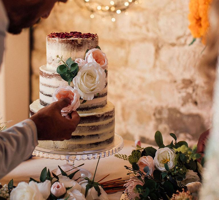 Three tier naked wedding cake complete with rustic styling and floral decor 