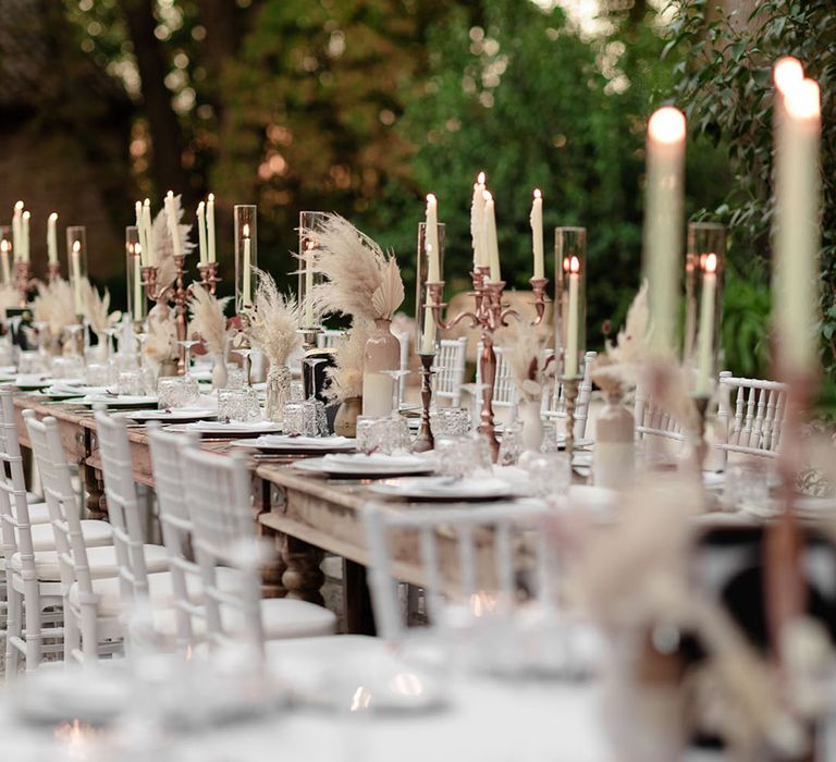 Rose gold candelabras line wooden banquet tables complete with pampas grass arrangements 