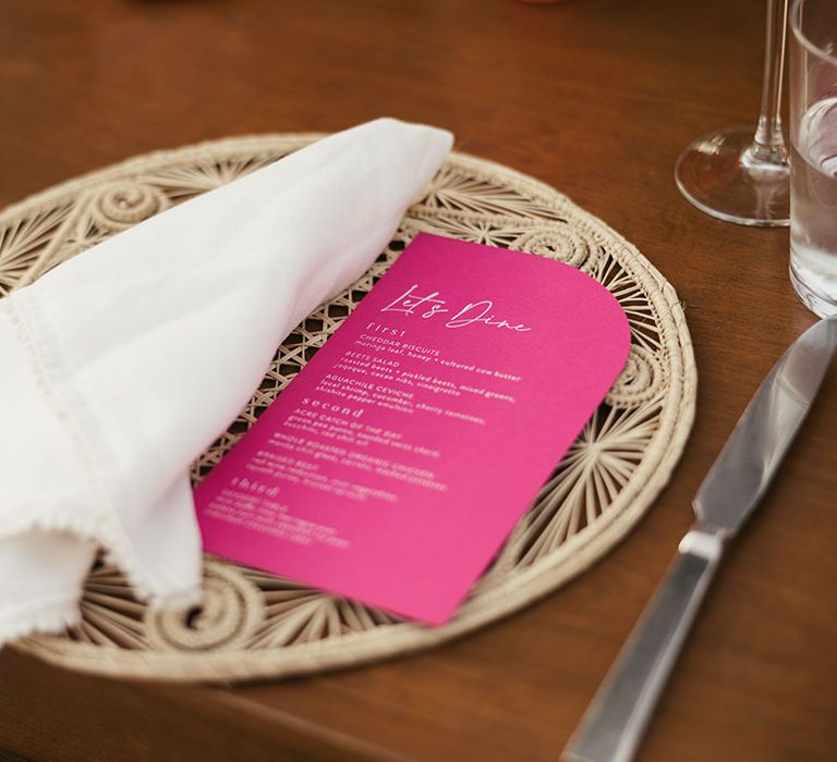 Bright pink menu beside white fabric napkin on place mat 