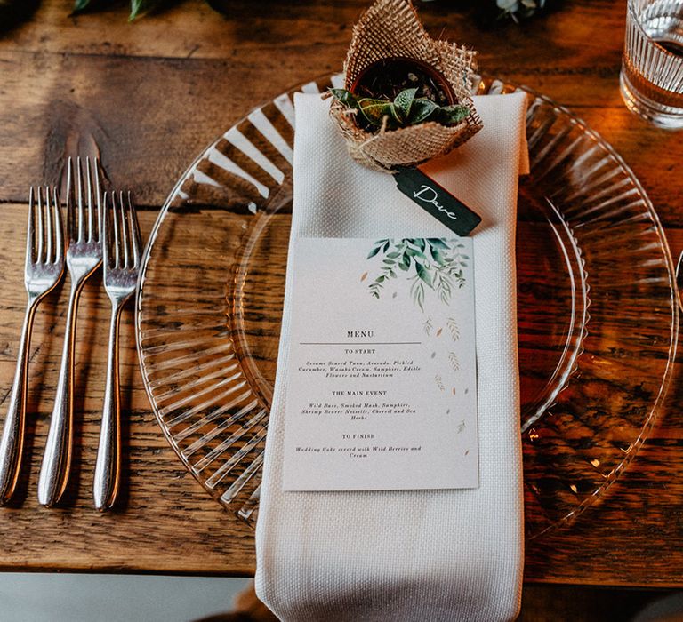 The wedding menu printed on a white card with green leaf design on a white napkin with DIY plant wedding favours 