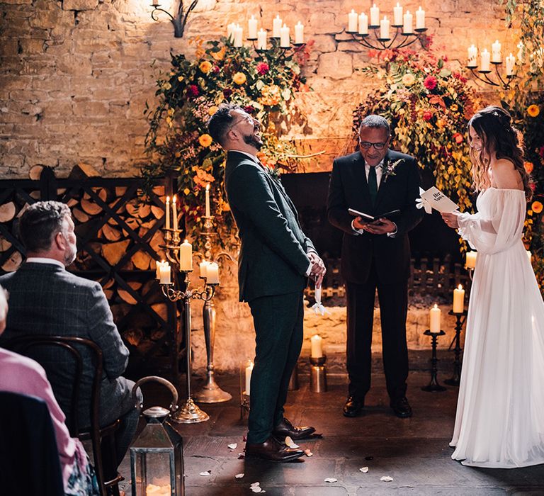 Groom laughing at the wedding ceremony standing facing the bride in an off the shoulder boho puff sleeve wedding dress 