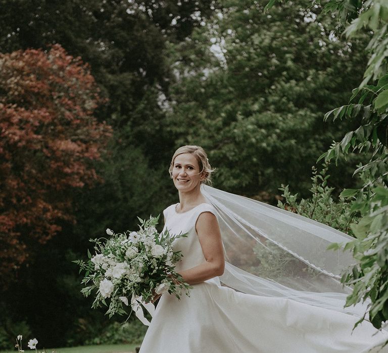 Bride in traditional high neck San Patrick wedding dress with embroidered veil carrying a large white wedding bouquet 