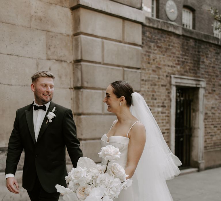 The bride holding her white wedding bouquet walks along with the groom for cute couple portraits together 