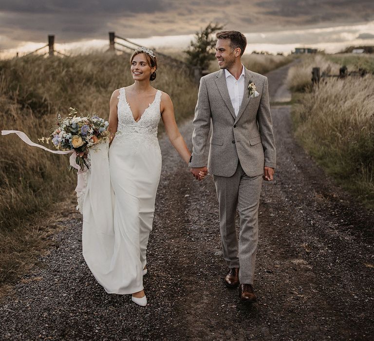 The bride and groom walk together under a dark cloudy and gloomy sky at their pastel theme botanical wedding 