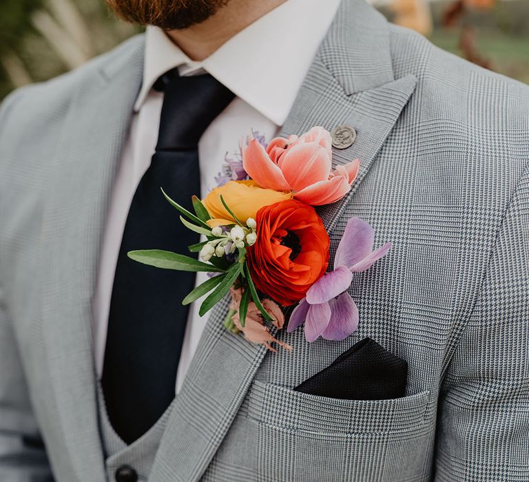 Groom wearing three piece wedding suit with navy tie with colourful large buttonhole 