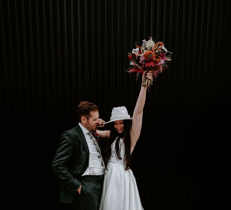 Bride in fun pearl bridal hat with the groom in dark green suit 