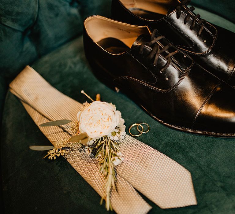 Groom's accessories with shiny black leather shoes, white flower buttonhole and cream tie 