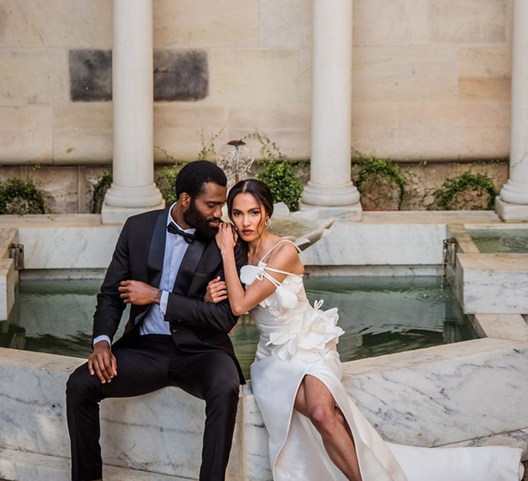 Destination wedding editorial shoot with the bride and groom seated next to fountain 