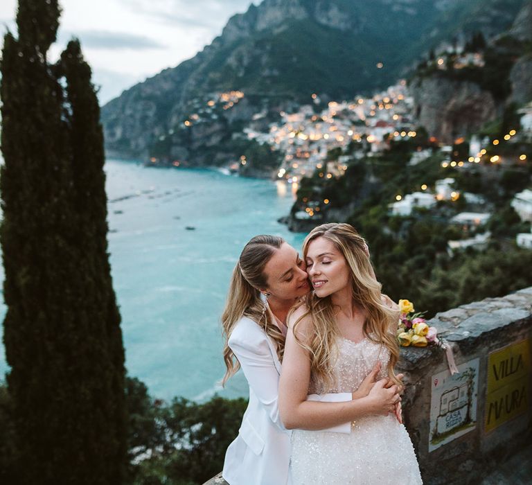 Two brides share a kiss at their elopement with the backdrop of Positano, Italy behind them 