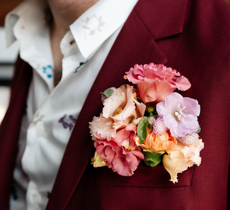 Pastel floral wedding buttonhole attached to the groom's burgundy wedding suit 