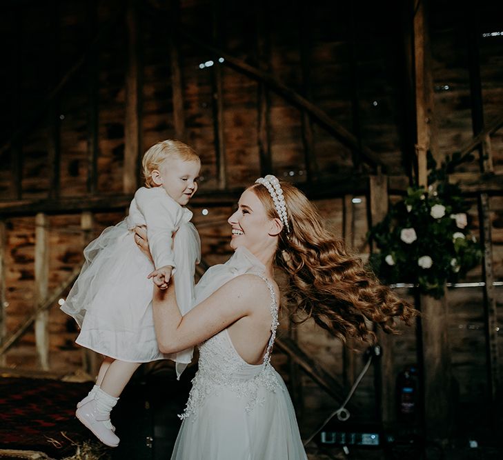 Bride with wavy hair and pearl headband swinging around the flower girl