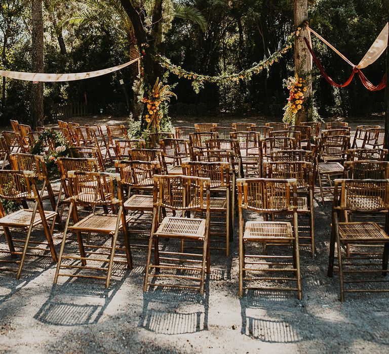 Outdoor forest wedding ceremony with wooden chairs and floral garland 