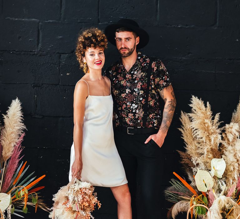 Stylish bride and groom with bride in short wedding dress and groom in floral shirt 