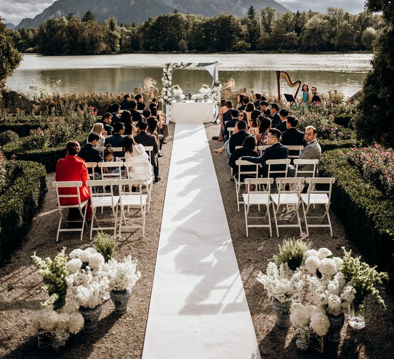 Outdoor wedding ceremony by a lake with wooden frame altar decorated in drapes and flowers 