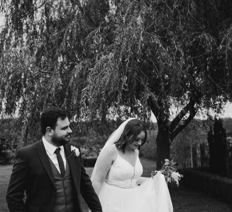 Bride with veil and lavender bouquet walking with groom in garden