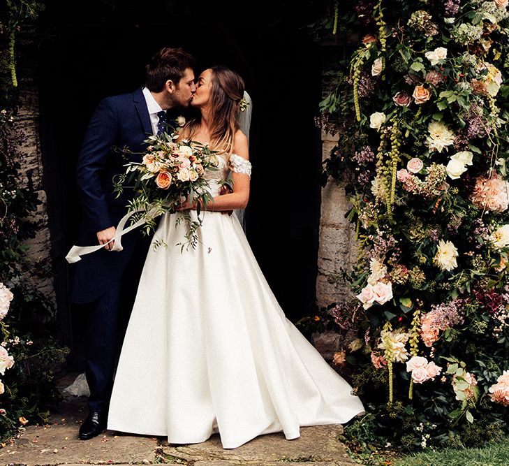 Newly wed couple kissing under flower arch 