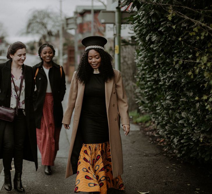 Stylish bride in fishtail dress with African print, trench coat and Zulu hat 