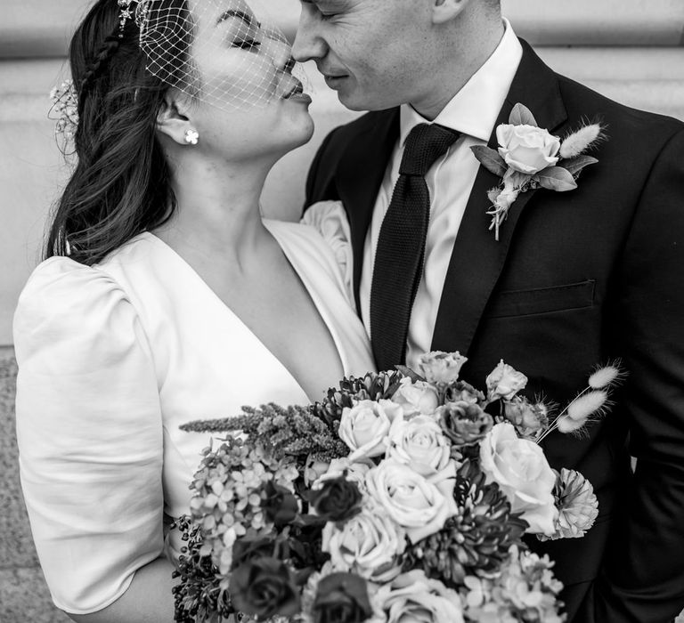 Black and white portrait of the bride and groom about to kiss with the bride wearing a birdcage veil