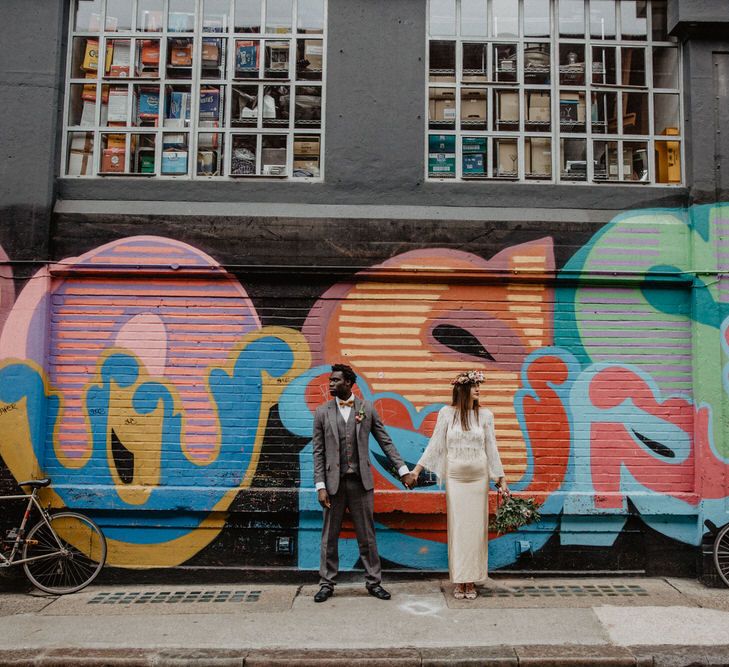 Wedding couple hold hands and look away from each other in front of vibrant graffiti wall