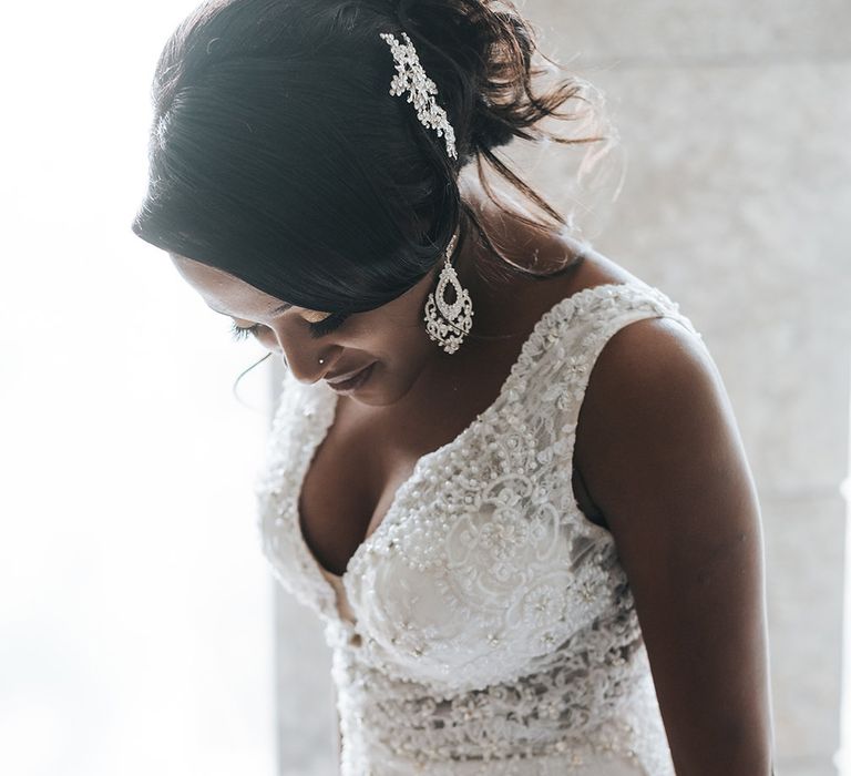 A Black bride looks down for a wedding portrait. She wears a nose stud and has statement earrings and a sparkly hair piece in her hair.