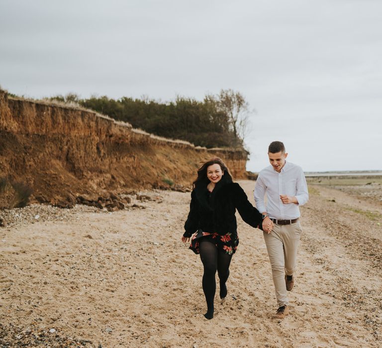 Portrait of the bride and groom-to-be running on the beach during their engagement session 