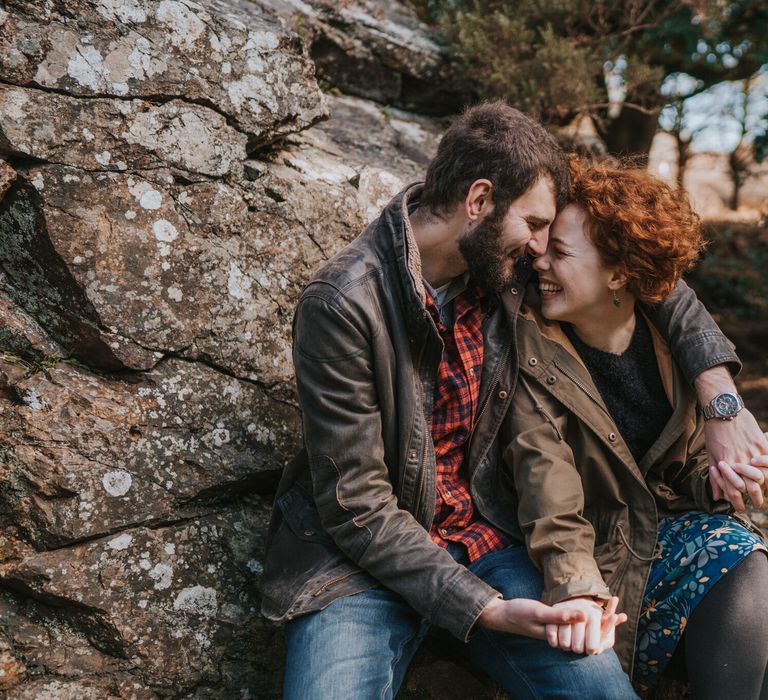 Couple look lovingly at one another whilst they sit together on rocks