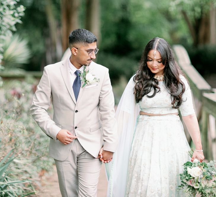 Groom in a sand suit and navy tie holding hands with his bride in a pastel green asian wedding dress