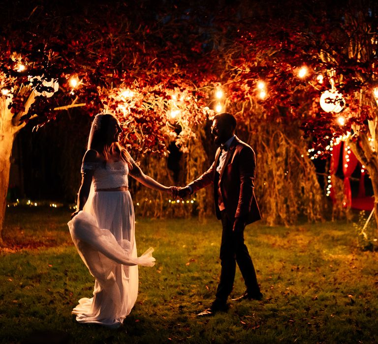 Bride & groom dance beneath trees lit up by lights