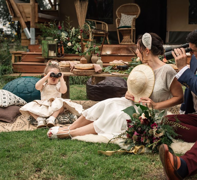 Bride & groom sit with little girl on the floor who plays with binoculars 