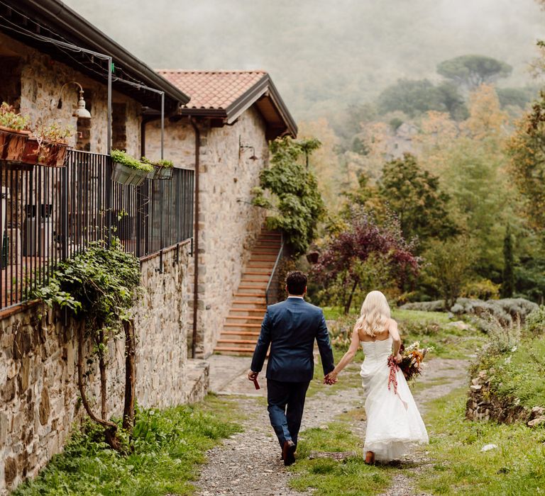 The bride and groom walk hand in hand through Podere Conti in Tuscany