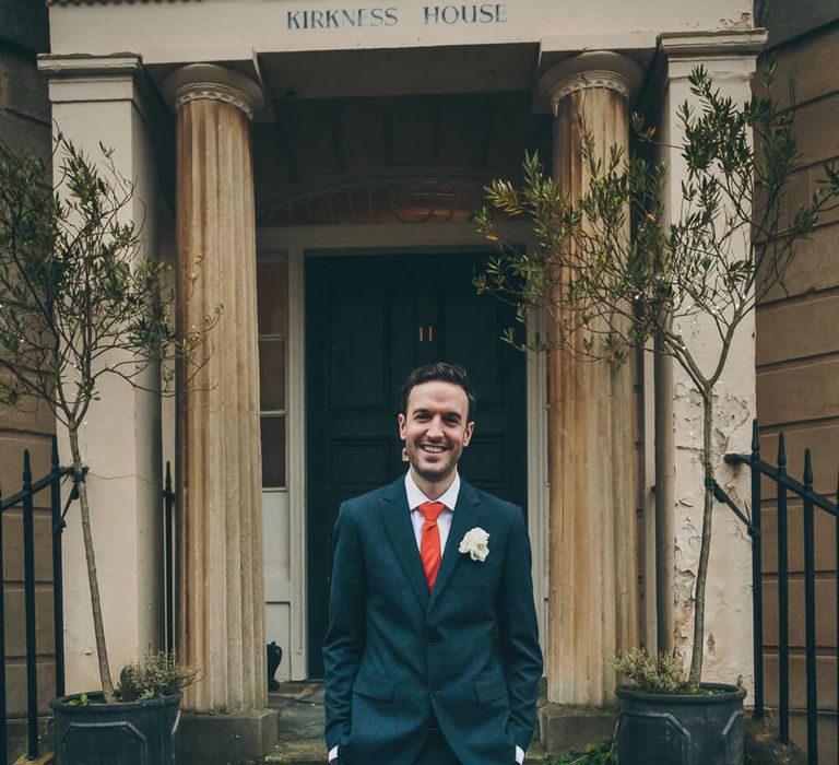 Groom stood outside bath wedding venue wearing red tie