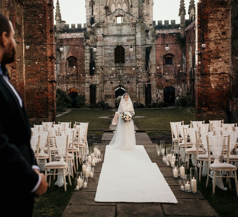 Groom in a black tuxedo standing at the altar waiting for his bride to walk down the aisle on a white carpet 