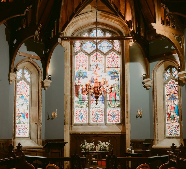 Church altar with stained glass window to the back and surrounded by white floral bouquets and chairs 