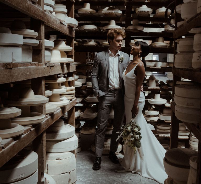 A bride laughs at her grooms as they stand in front shelves of ceramics. She holds a white dried flower bouquet down to her side for a simple elegant wedding. 