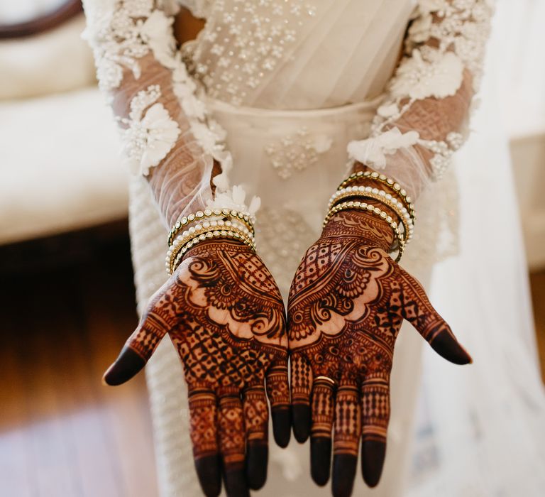 Bride shows her mehndi whilst wearing gold and pearl bracelets on her wedding day