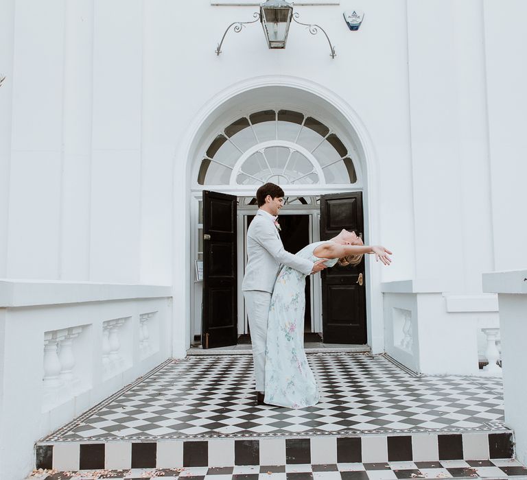 Groom leans back bride on the day of their wedding in front of the doors of the Belair House