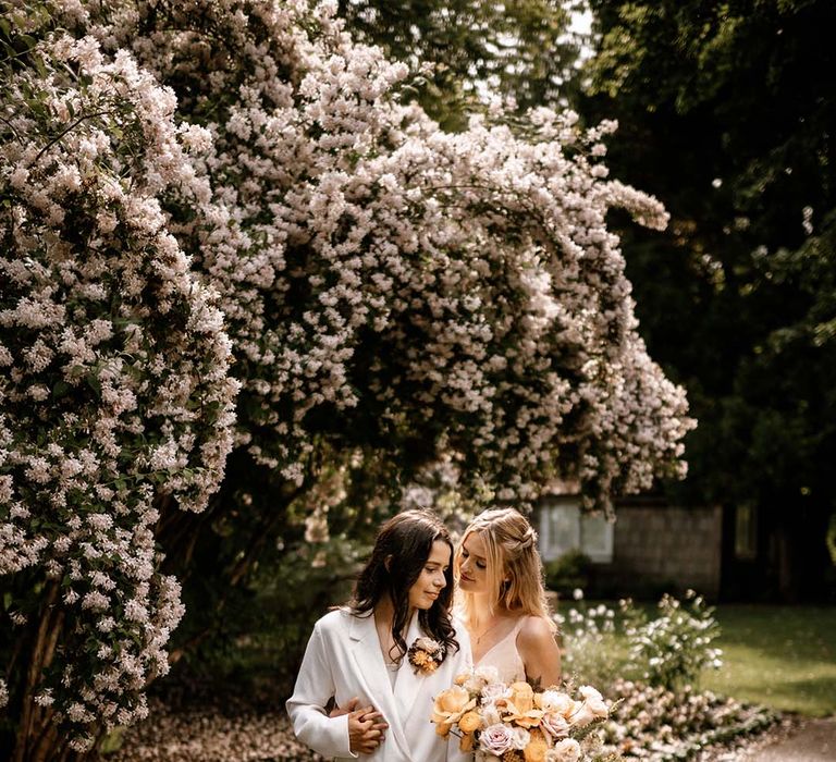 Couples portraits under a blossom tree with bride in a white suit and blush wedding dress