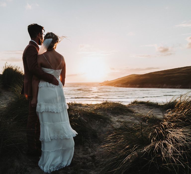 Bride & groom watch the sunset with one another on the beach together in Cornwall on their wedding day