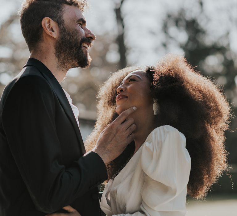 Groom smiling with his bride in a long sleeve wedding dress with afro hair 