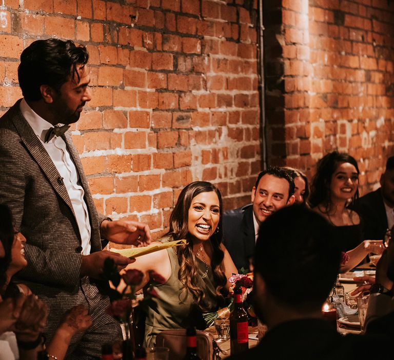 A groom stands to make a speech at industrial wedding venue.