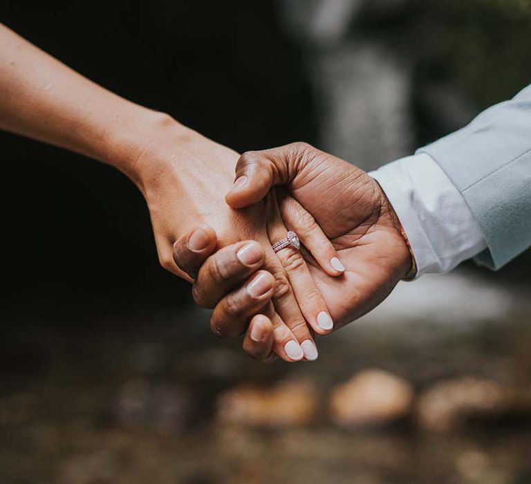 Close up image of bride & groom holding hands complete with brides pear shaped engagement ring diamond